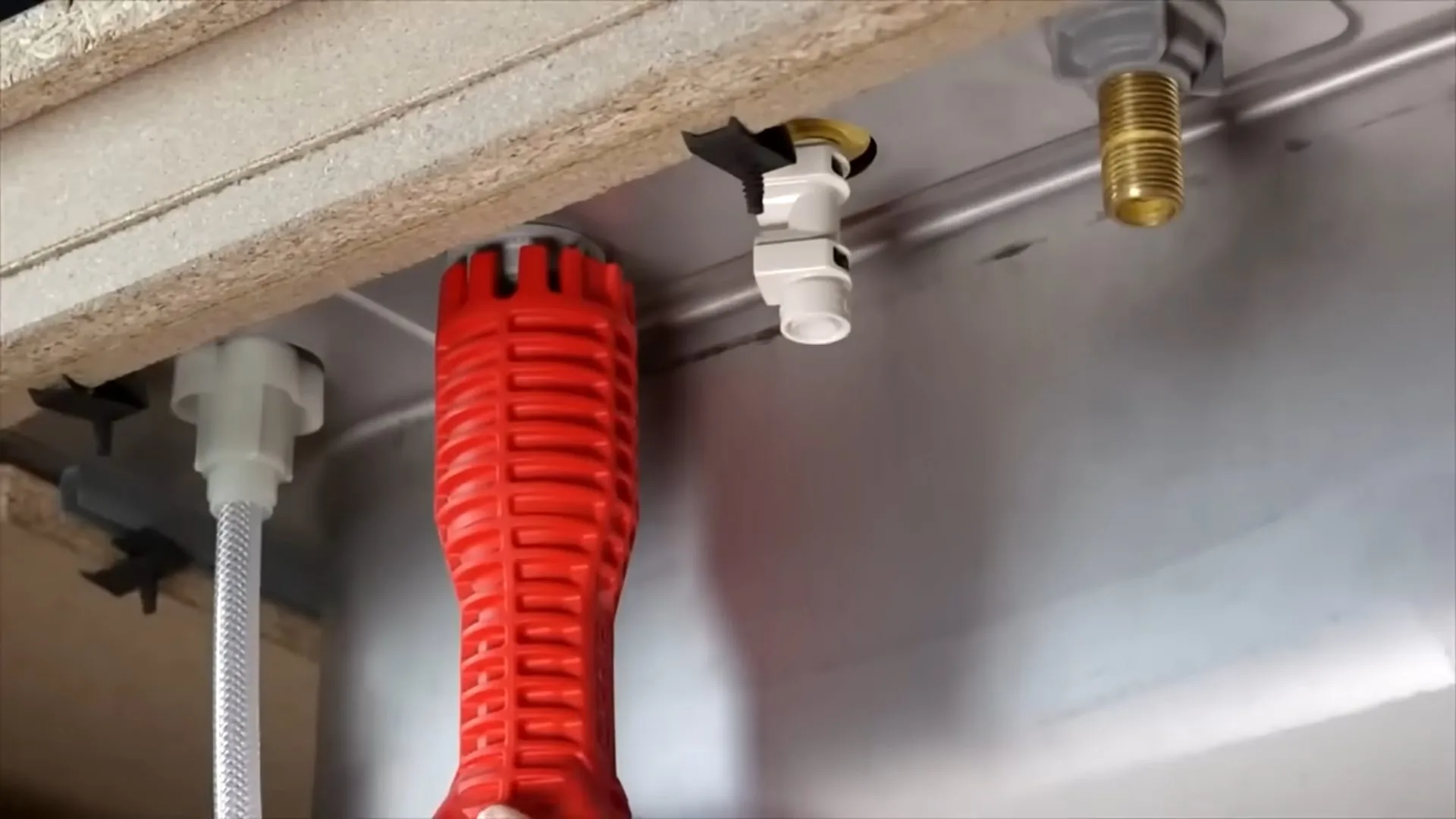 Red basin wrench and white supply lines seen from beneath a steel sink