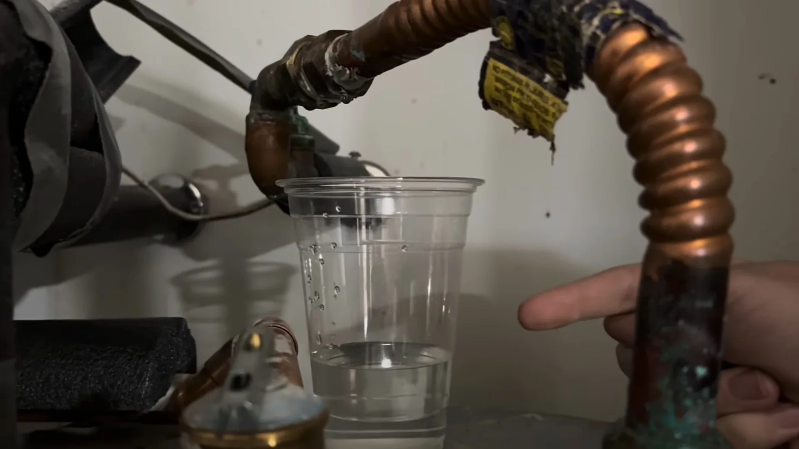 Green-corroded copper pipe dripping into a clear plastic cup
