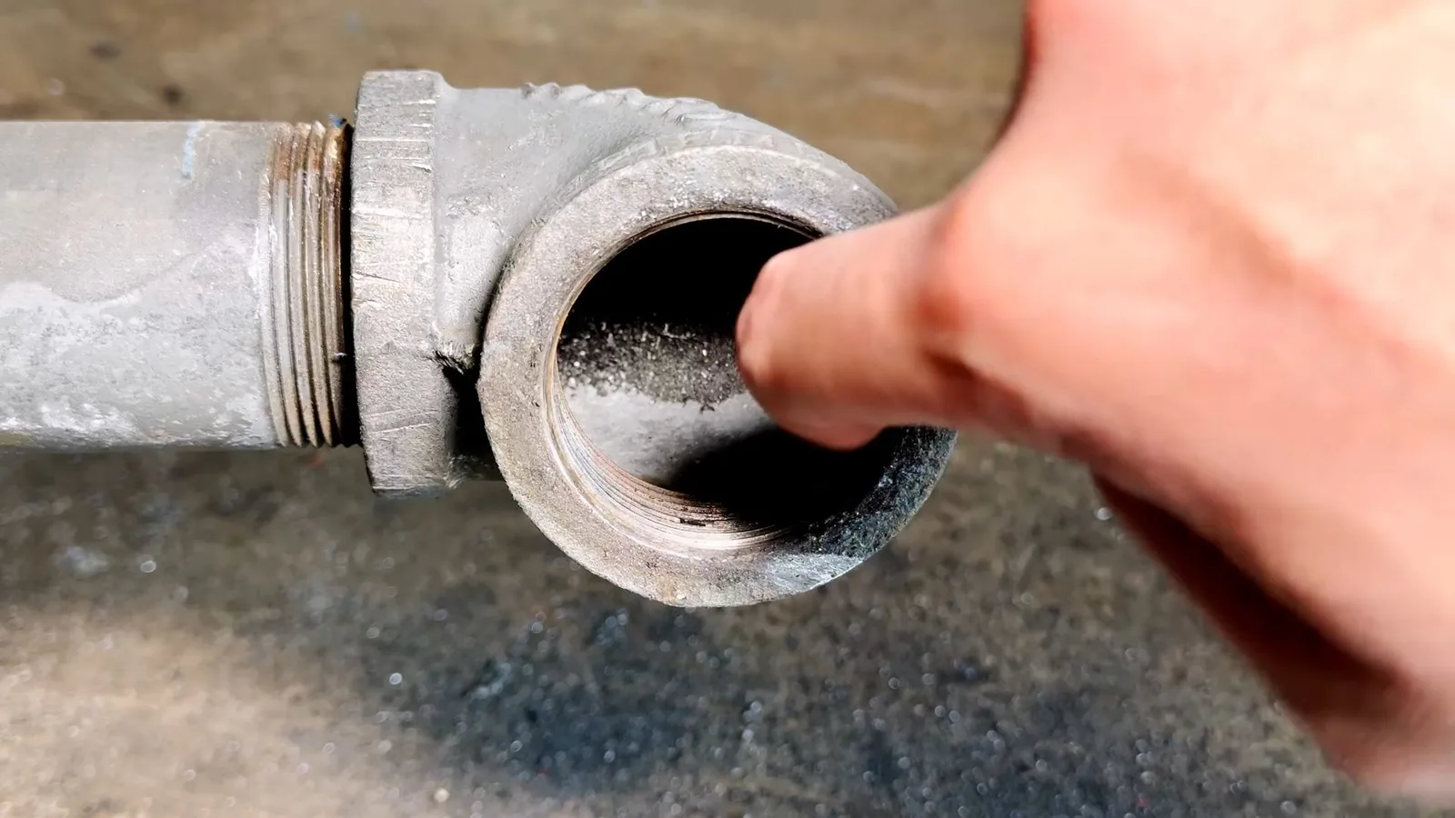 Fingertip pressed against scale buildup inside a galvanized pipe elbow