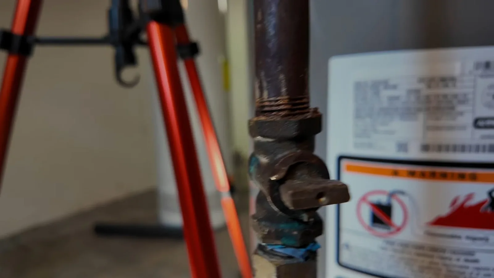 Black iron gas shutoff valve beside a water heater with a warning label on the tank