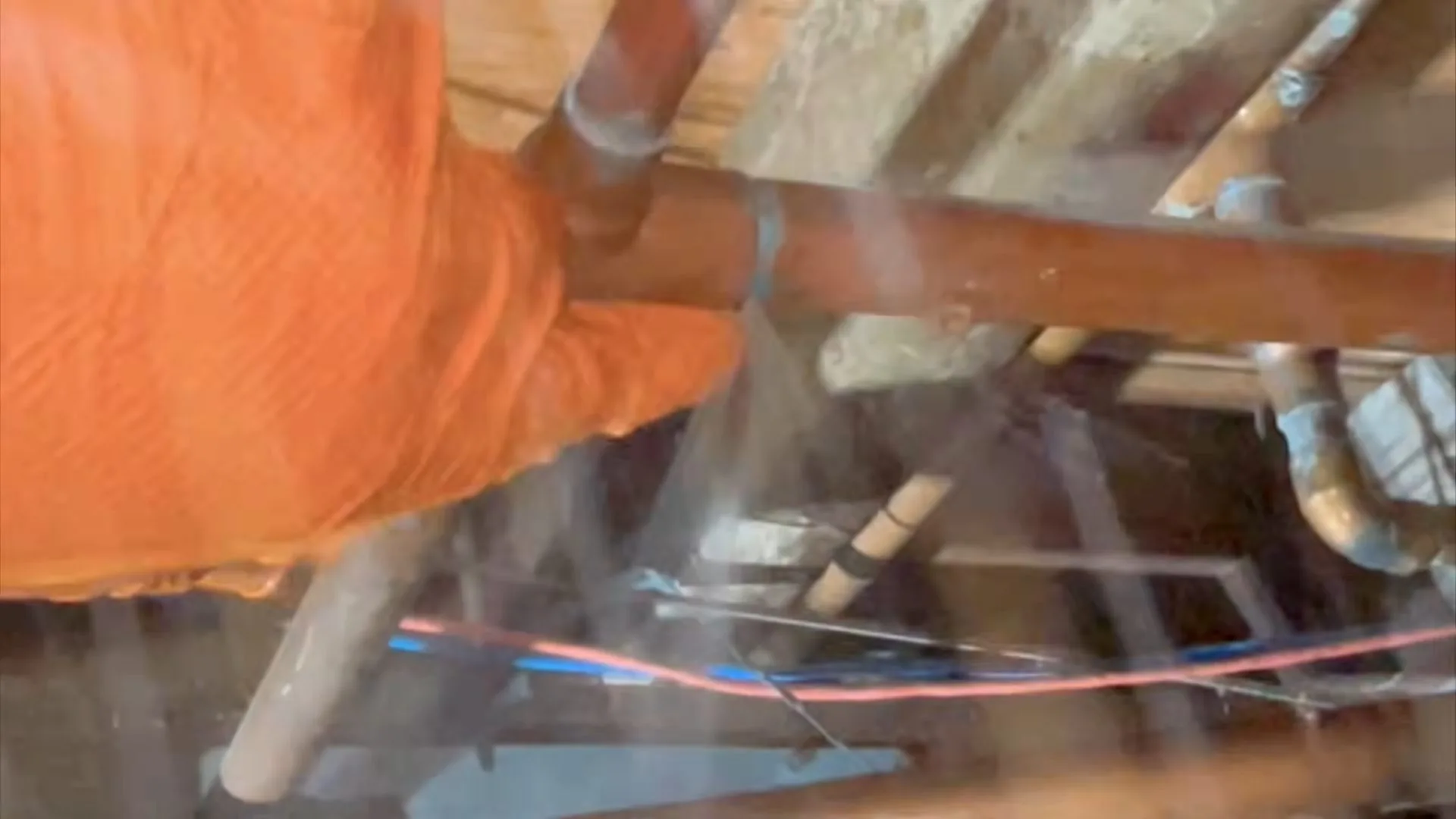 Gloved hand held over a copper pipe spraying water between wall framing