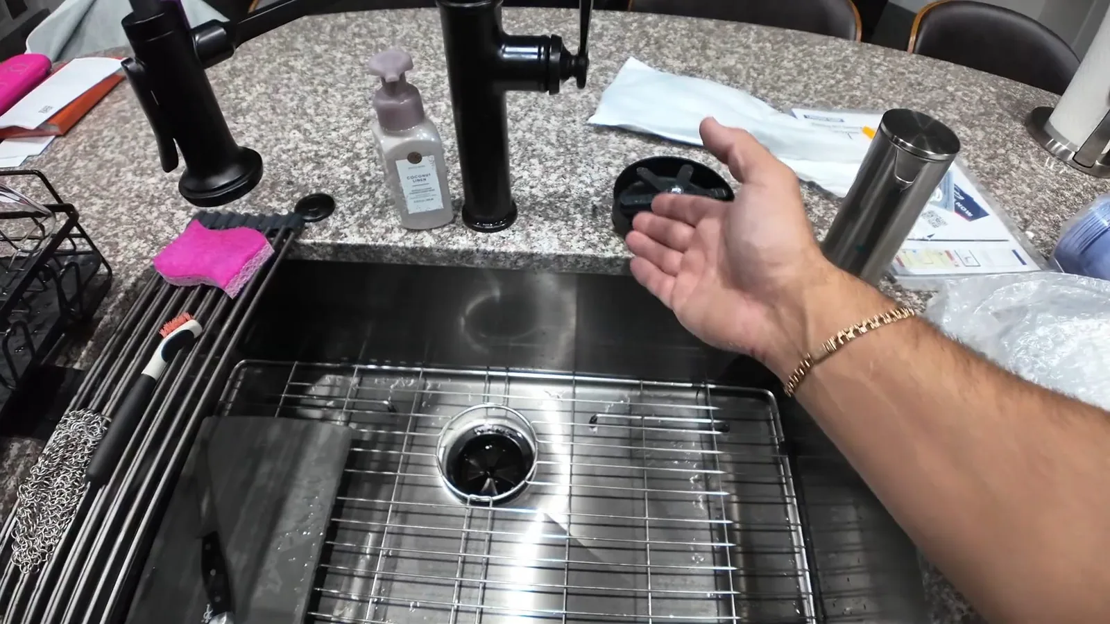 Hand held over the disposal opening in a stainless steel sink with a grate