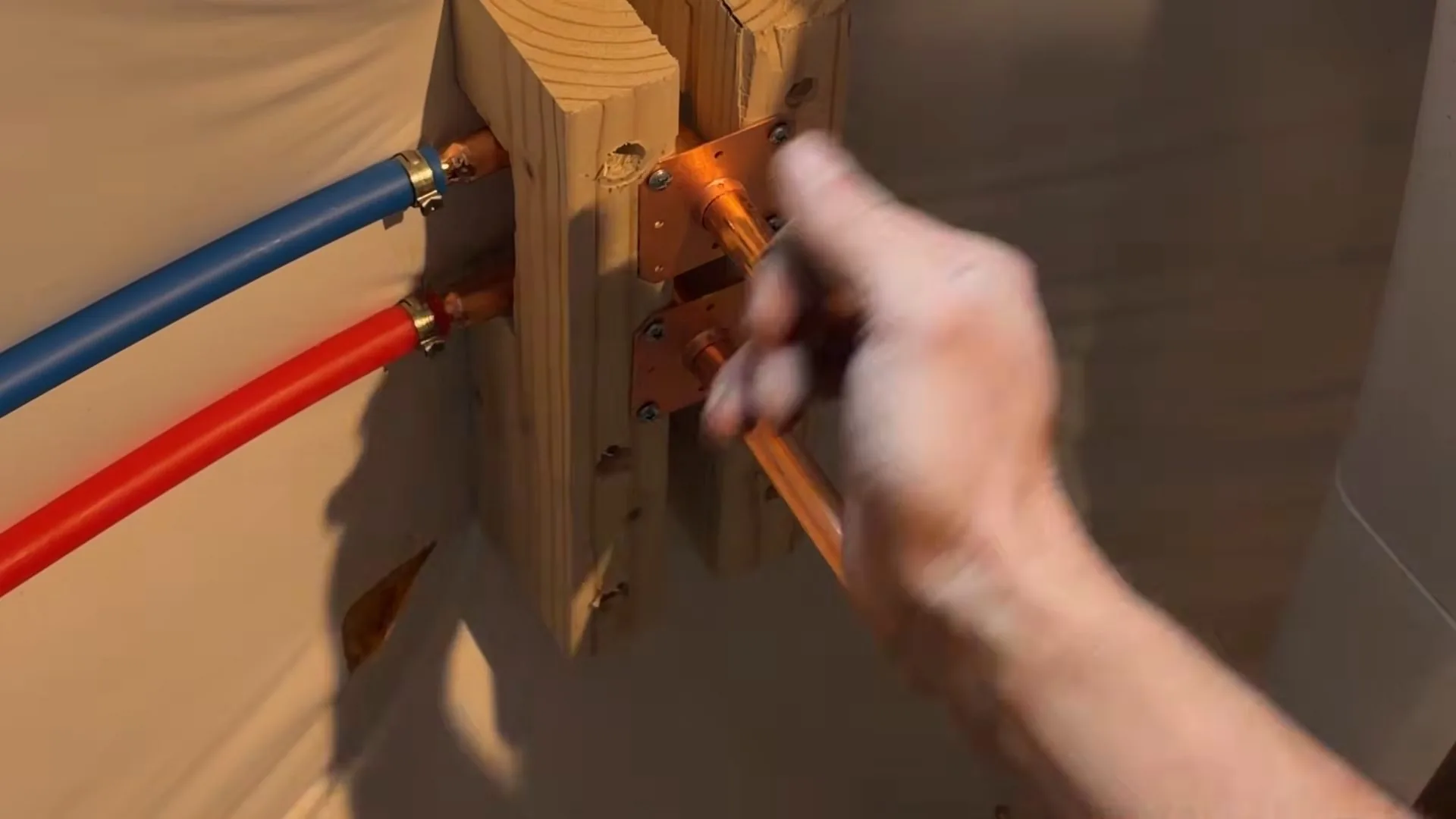 Hand at red and blue PEX tubing connected to brass fittings on a wooden mounting block