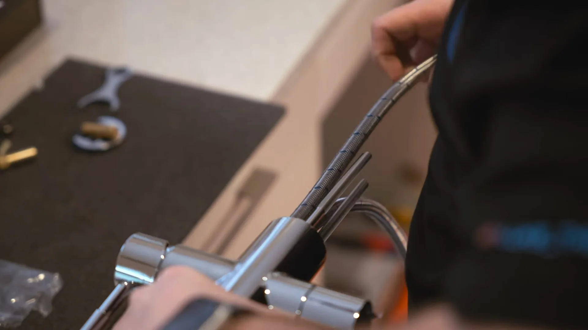 Hands working a supply line and tools beneath a kitchen counter during a faucet install