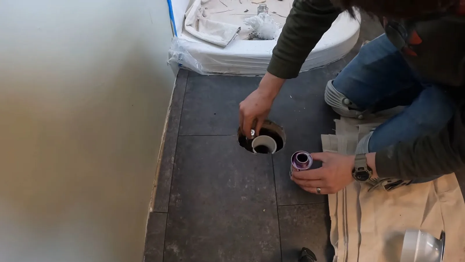 Person kneeling on a subfloor setting a toilet flange over an open drain pipe