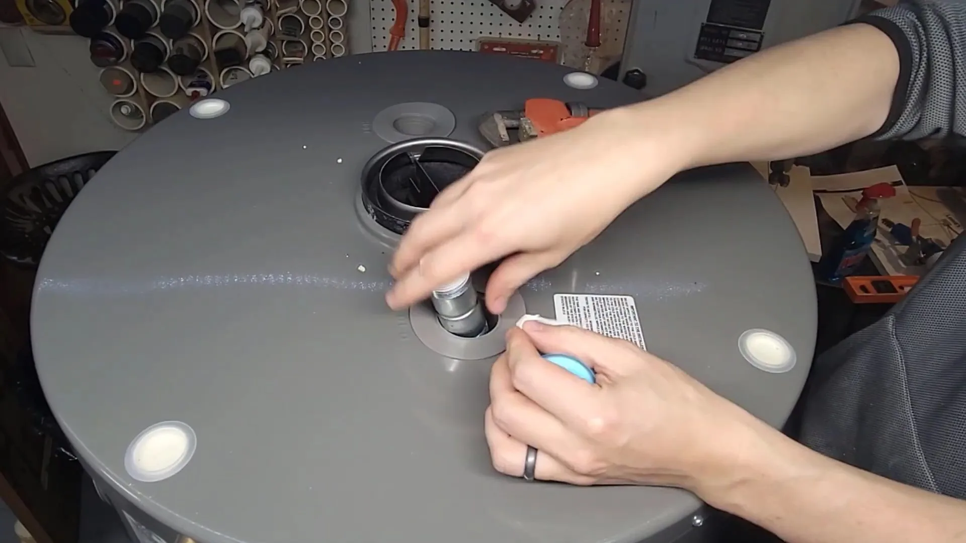 Two hands working at the fitting on top of a gray tank water heater