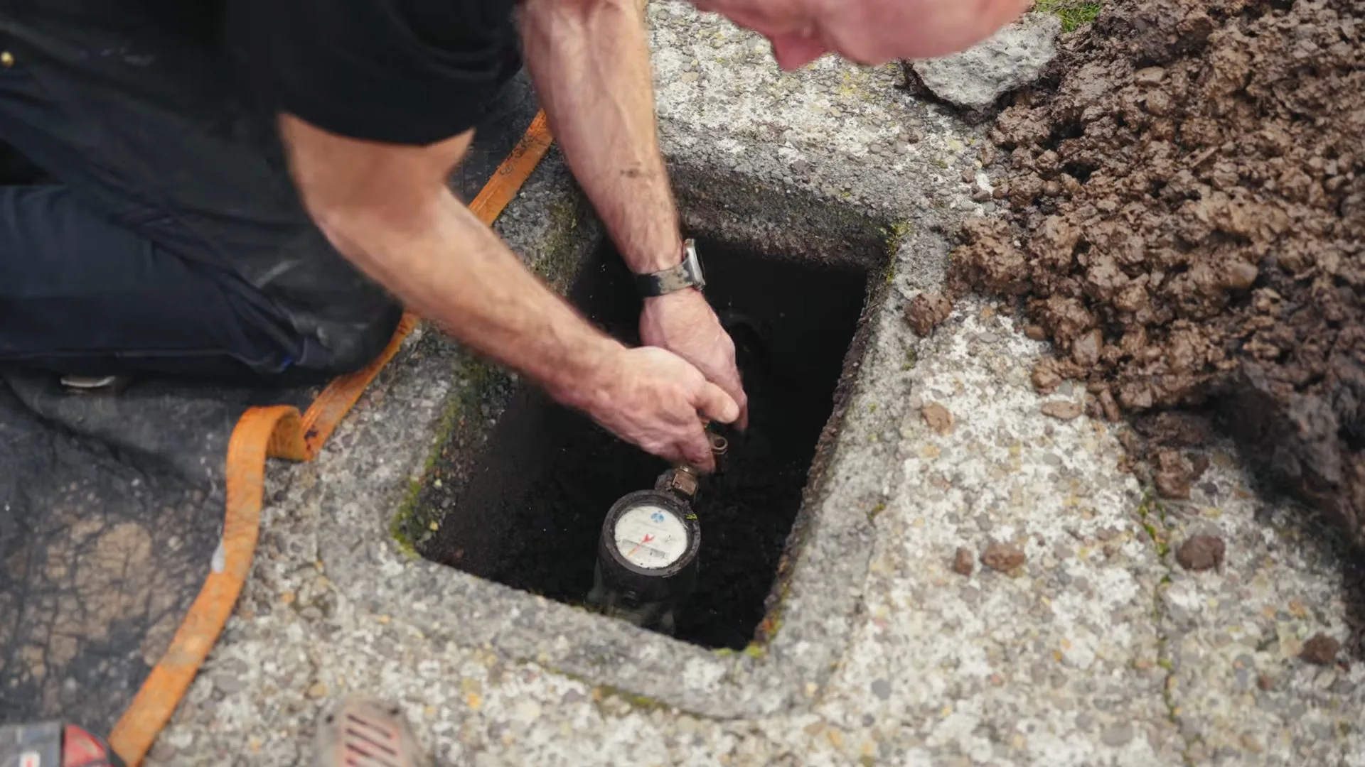 Man crouched at an in-ground meter box reading a water meter