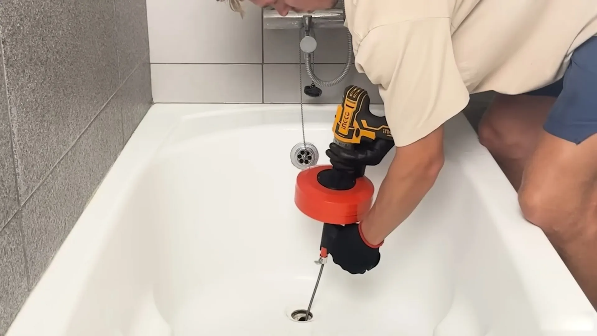 Man feeding a drill-driven drain cable into a bathtub drain