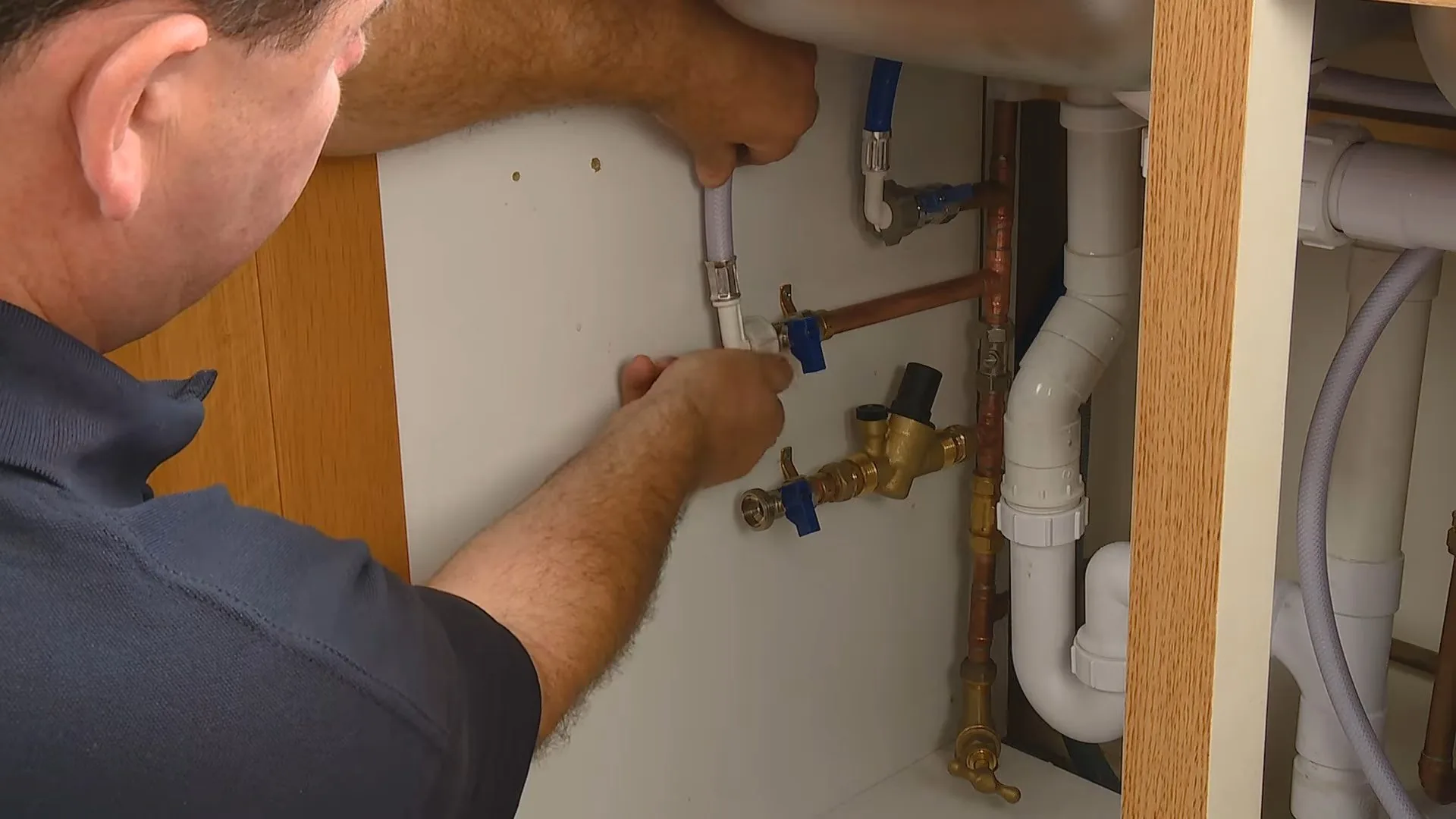 Man reaching under a sink to work on copper supply lines and angle stop valves