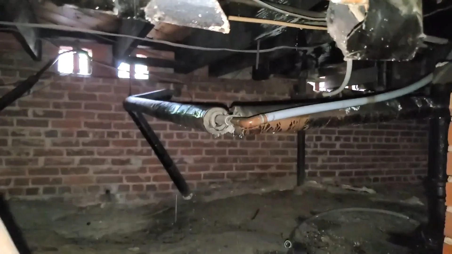 Dark brick-walled crawlspace with a black cast iron pipe and water dripping from a fitting overhead