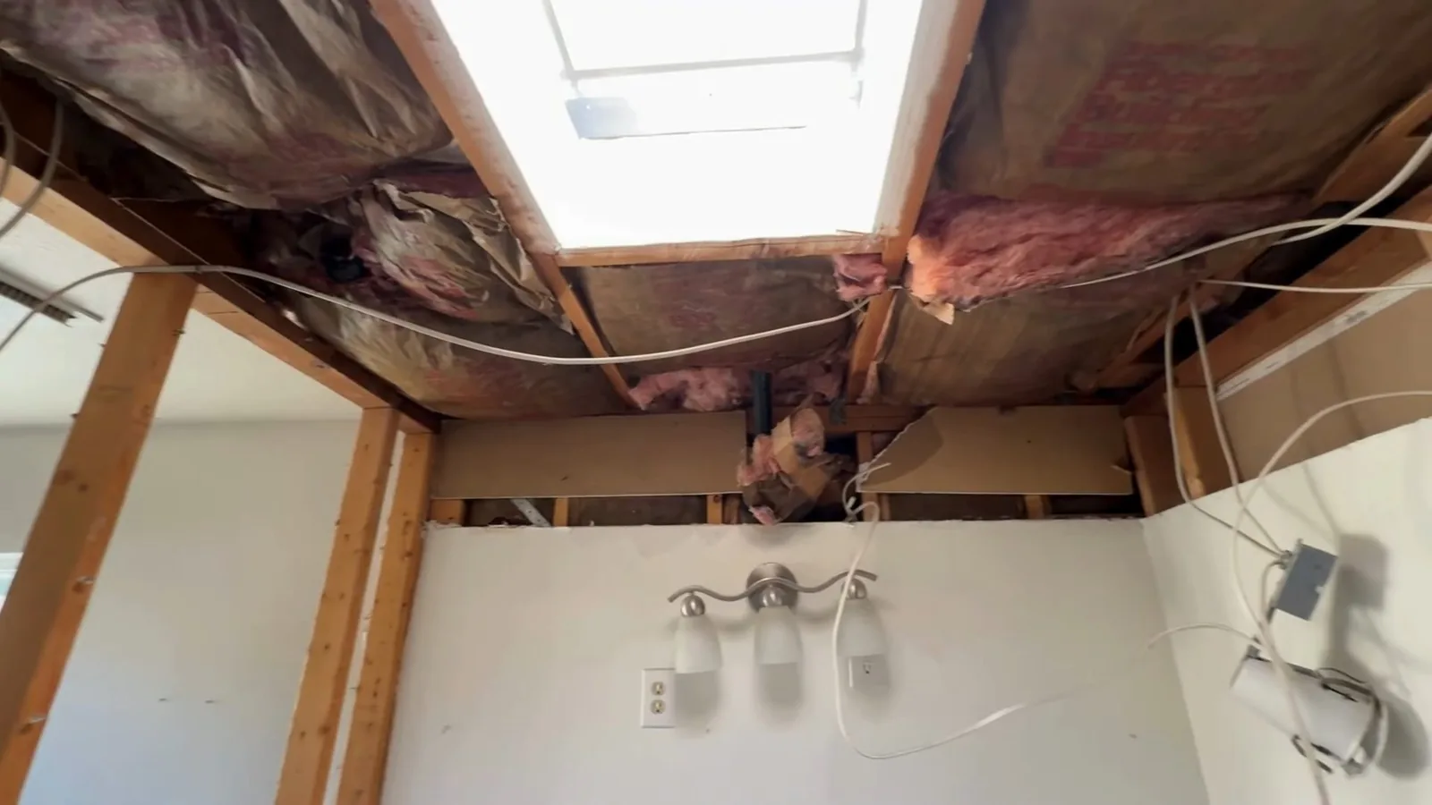Opened ceiling with insulation and framing above a bathroom vanity light