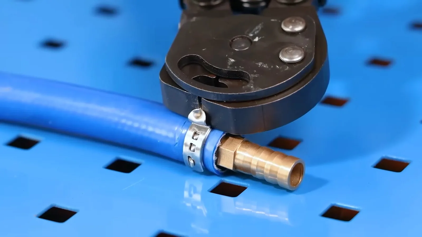 Crimp tool clamped on a blue PEX tube at a brass fitting on a blue workbench