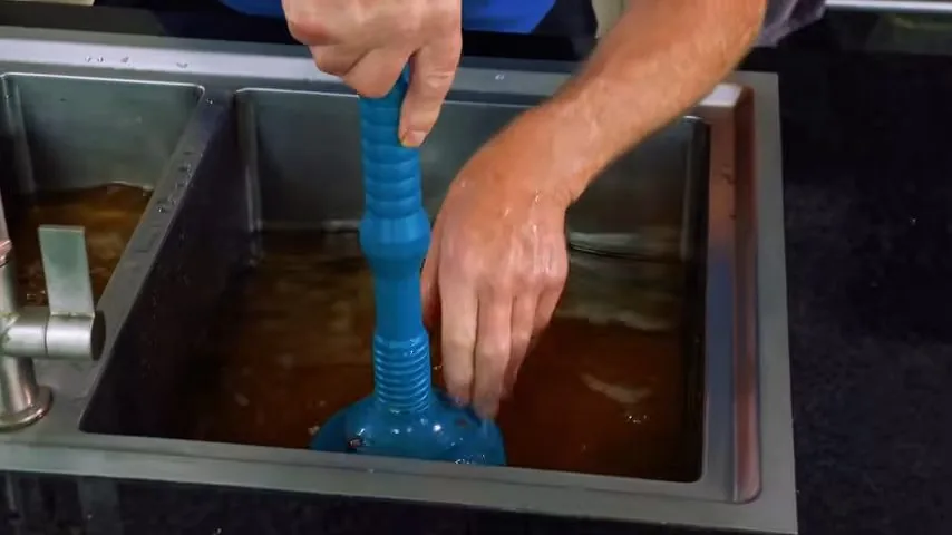 Blue plunger pressed into a stainless sink holding brown water