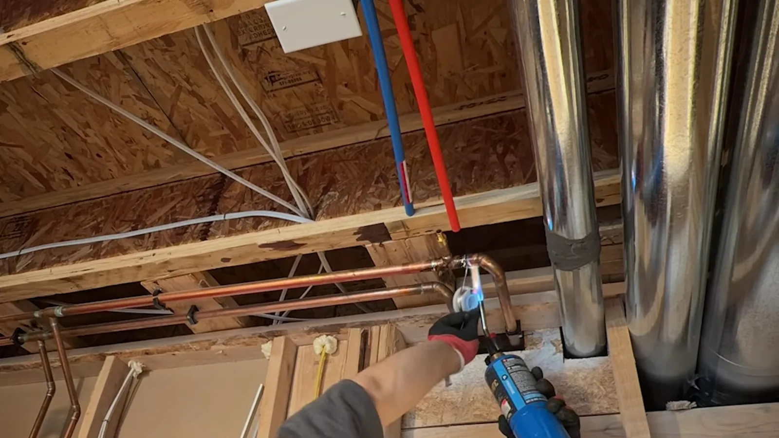 Basement ceiling joists with copper pipe being soldered beside red and blue PEX lines