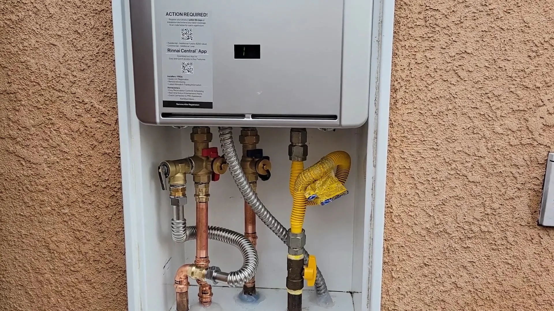 Wall-mounted tankless water heater in a recessed box with gas, water and valve connections below it
