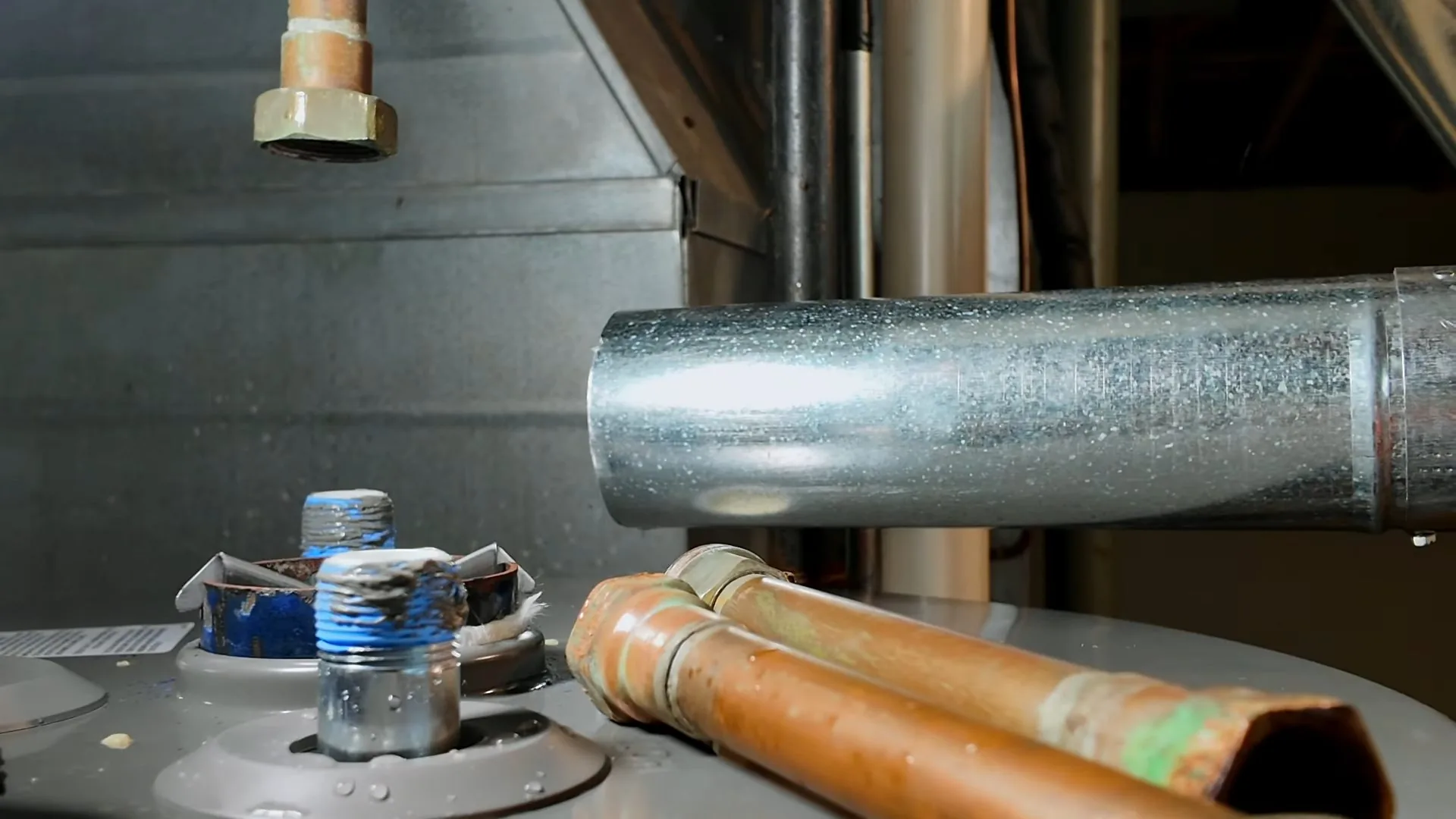 Top of a tank water heater with a metal flue pipe, copper supply lines and threaded fittings