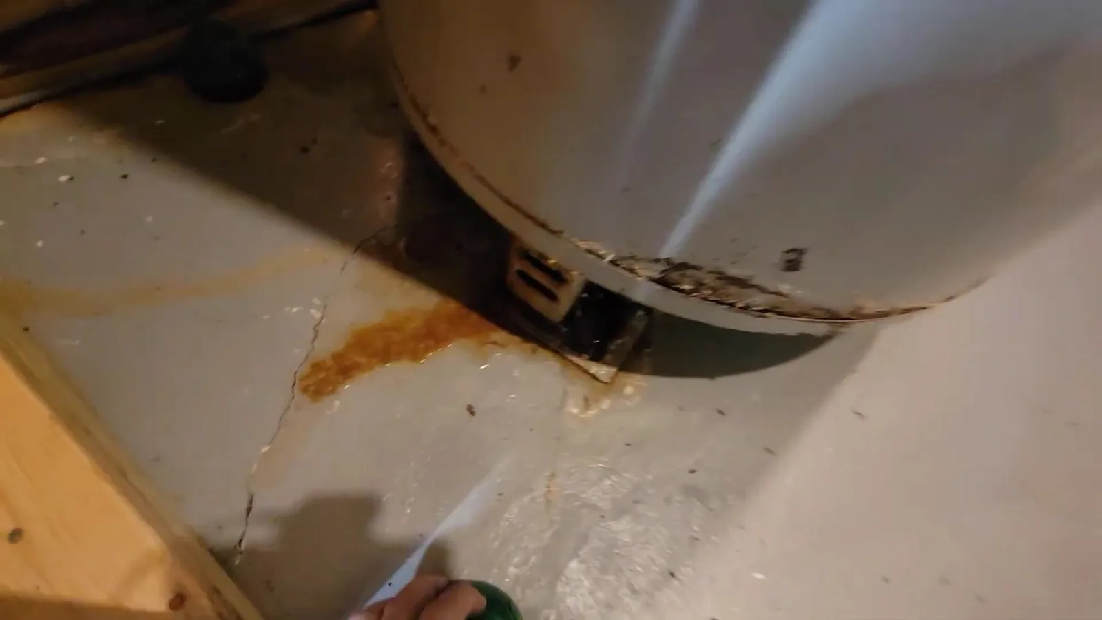 Rust-stained base of a water heater with water spraying onto the floor beneath it