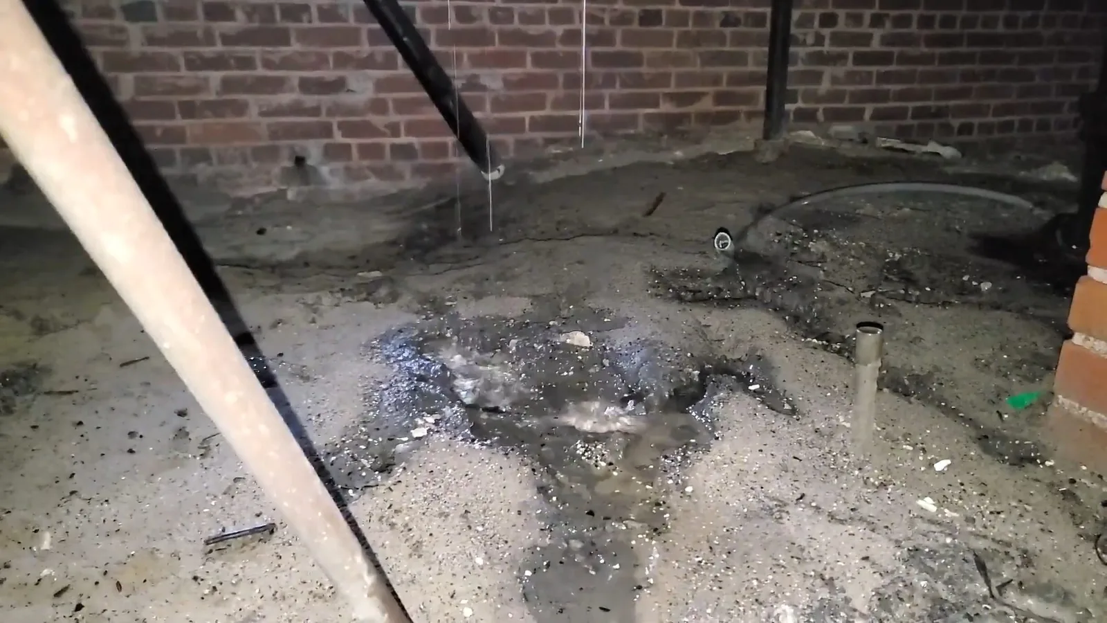Wet, stained ground in a crawlspace under a house with water dripping from a pipe above